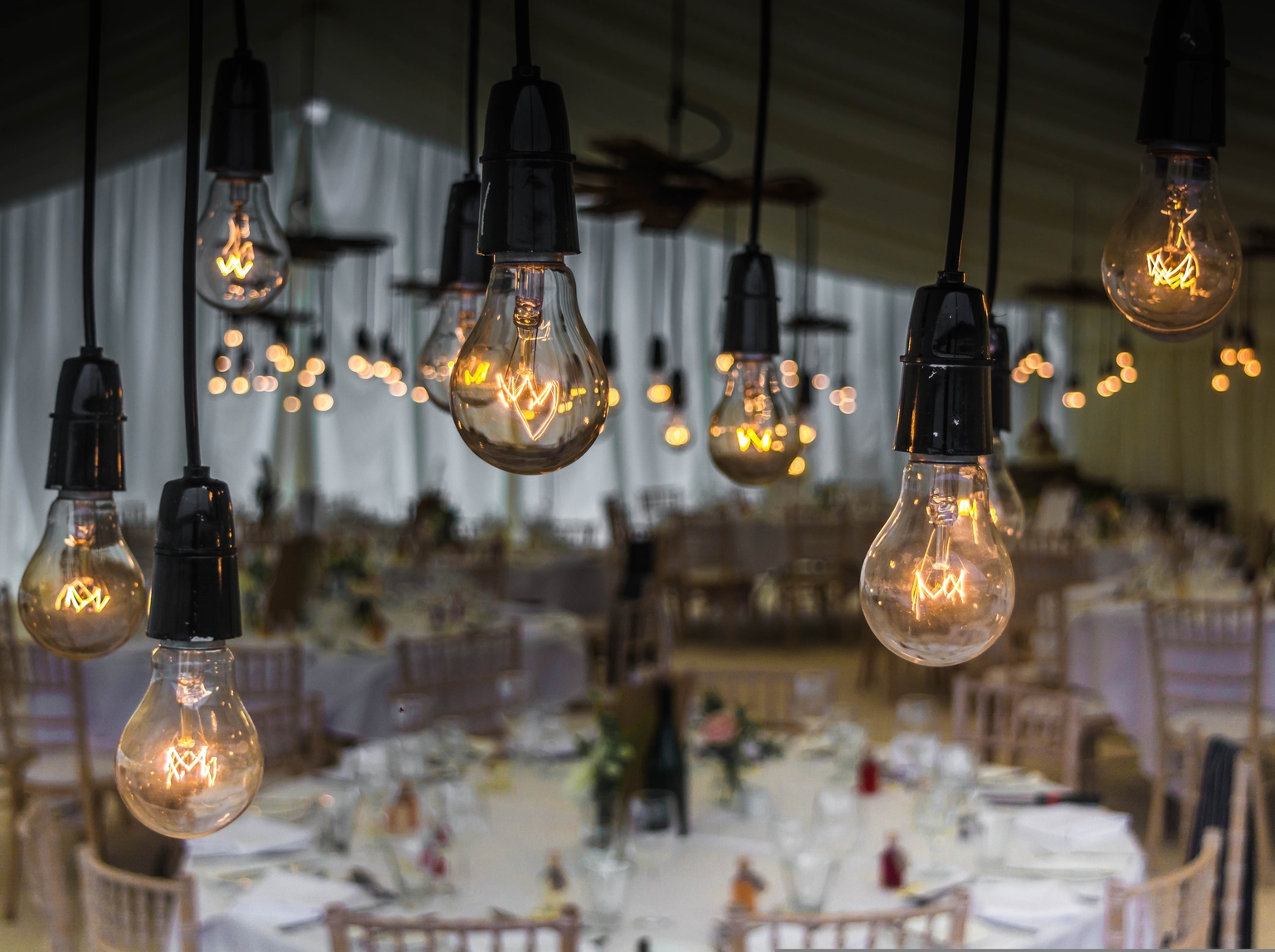 Banquet hall set for a wedding or function, with warm Edison bulb lighting and dressed tables